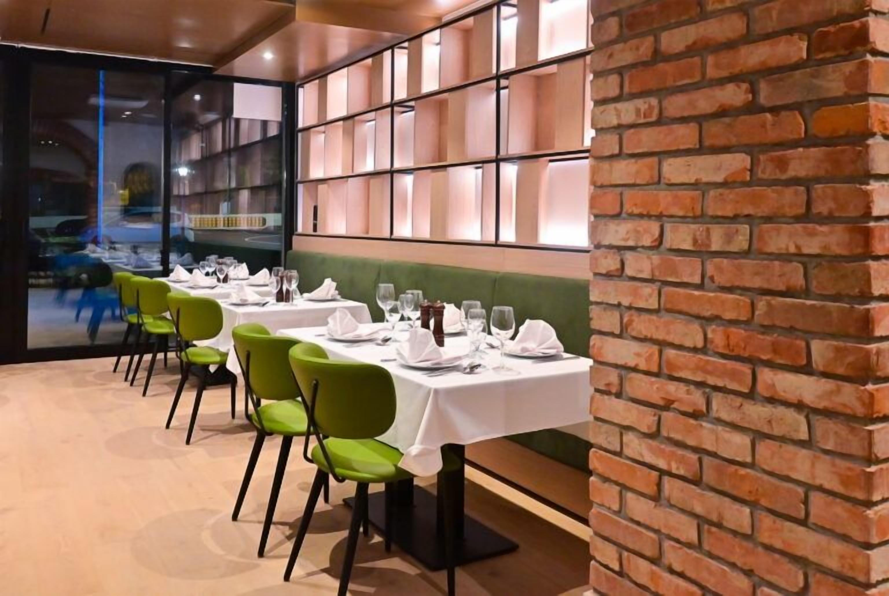Un restaurante con mesas dispuestas para comer, sillas verdes y una pared de ladrillo.