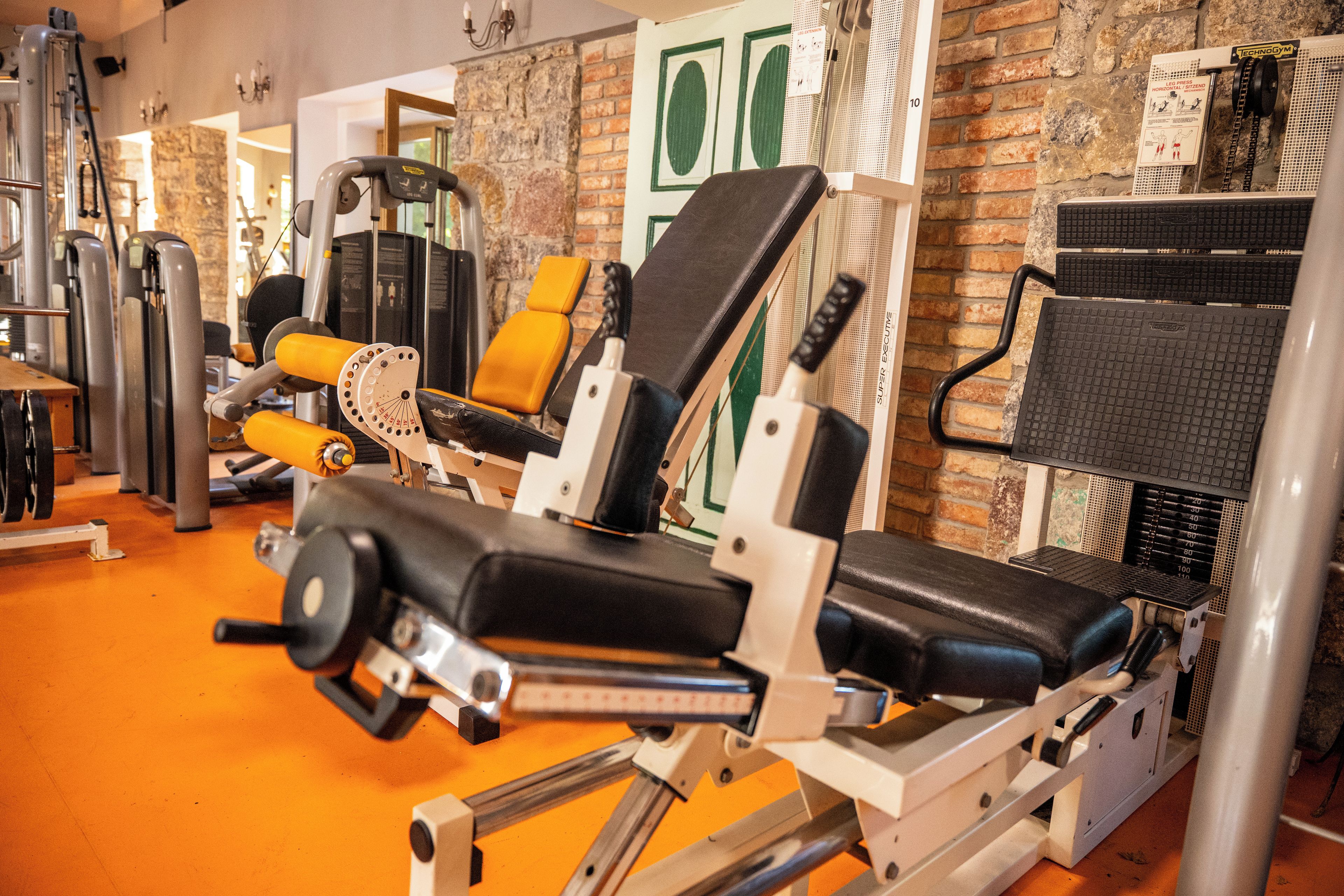 A gym with various exercise machines and a brick wall backdrop.