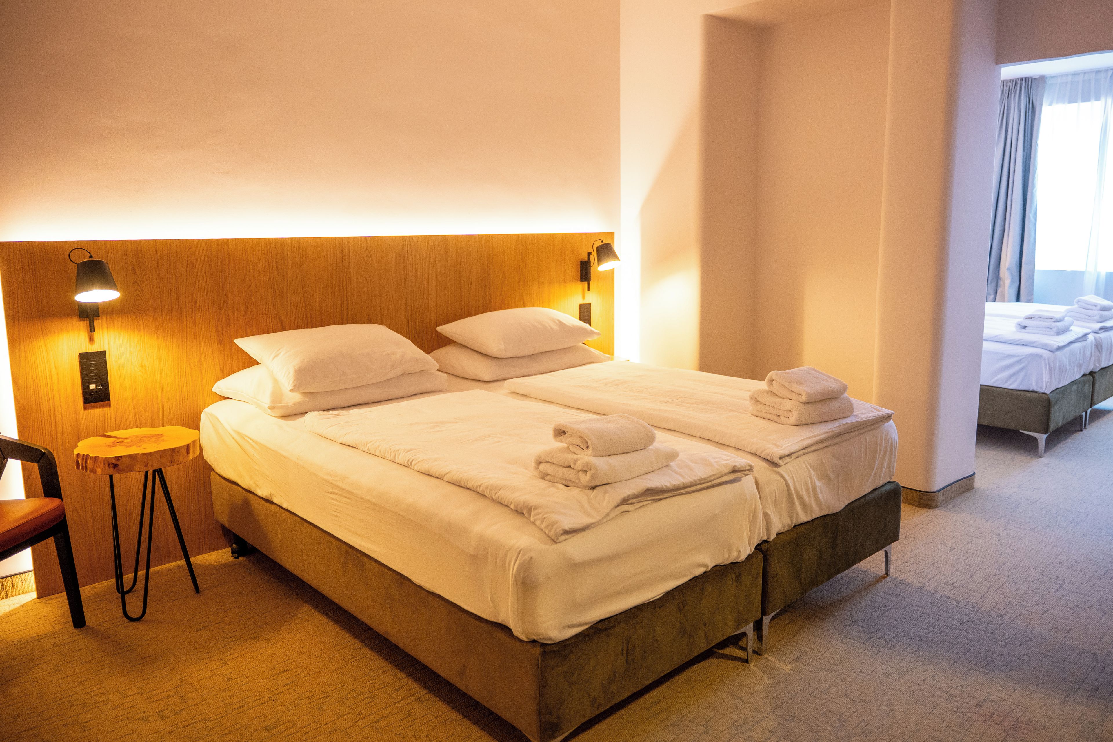A hotel room with a large bed, two bedside lamps, a wooden headboard, and a small round table.
