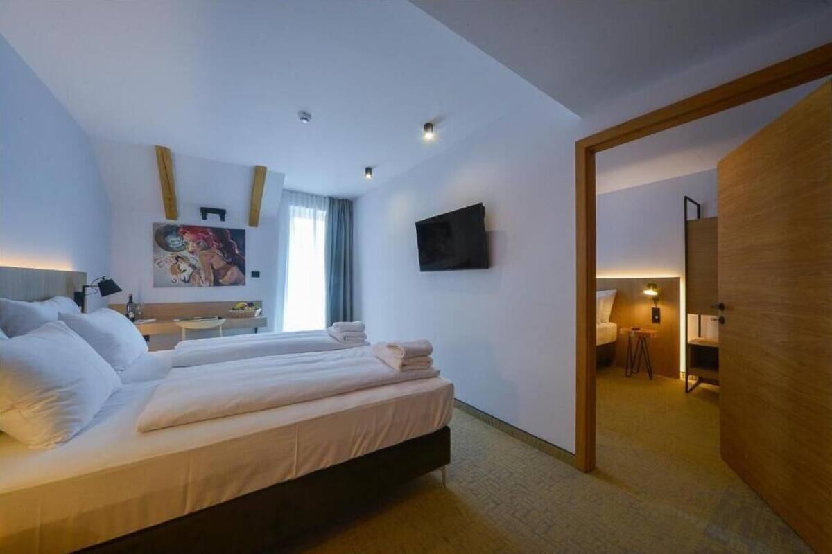 A hotel room with a bed, a desk, a TV, and a painting on the wall.