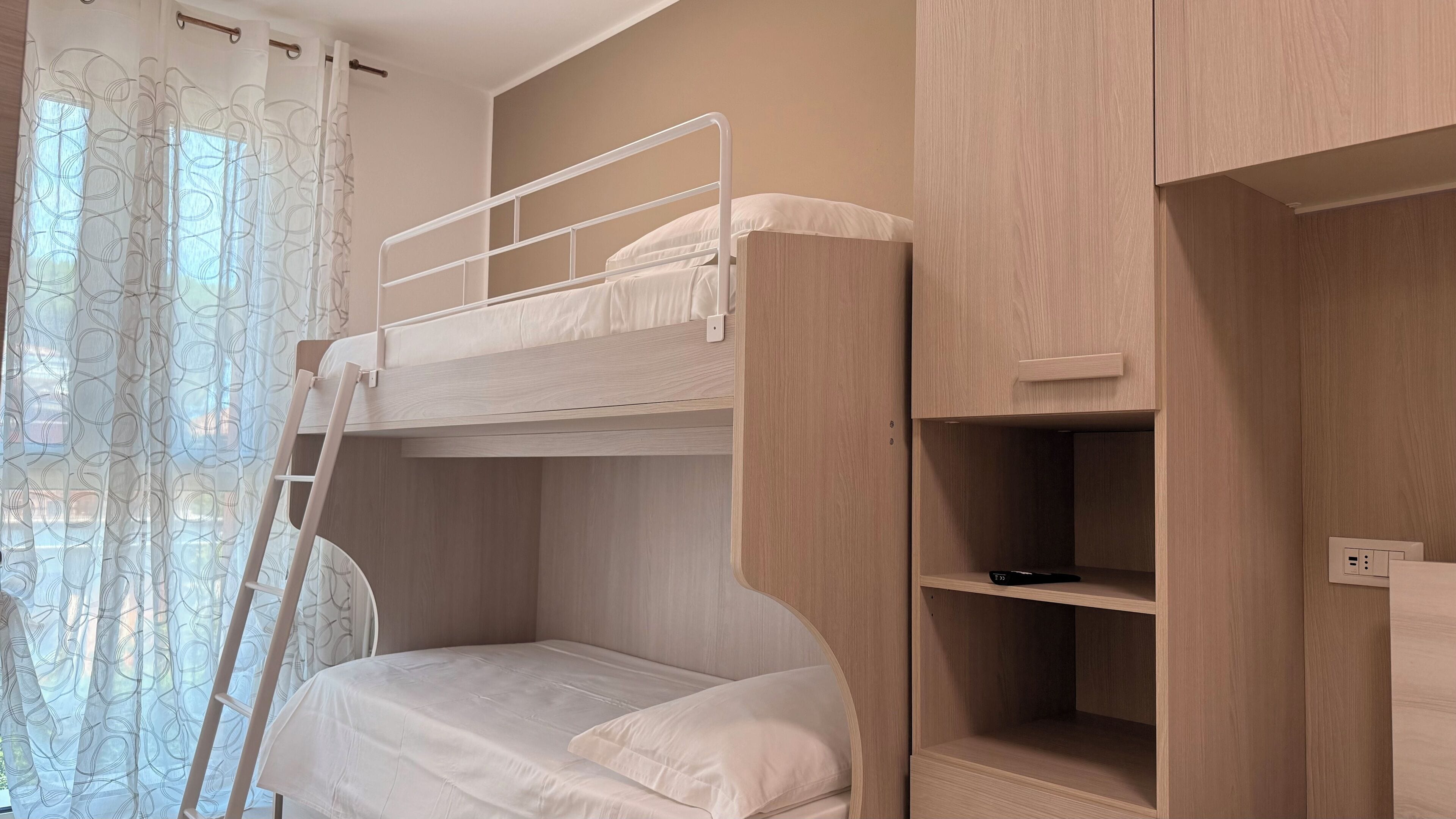 A bunk bed with a ladder, a bedside table, and a shelf unit with a power outlet.