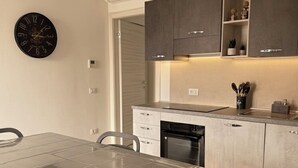 Een moderne keuken met een eettafel, stoelen, kastjes en een klok aan de muur.