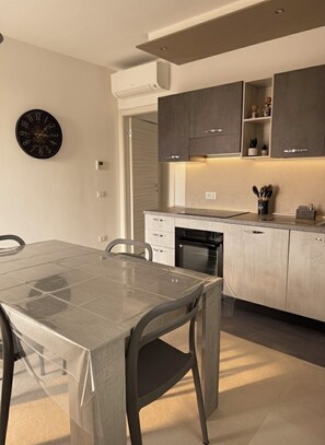 A modern kitchen with a dining table, chairs, cabinets, and a clock on the wall.