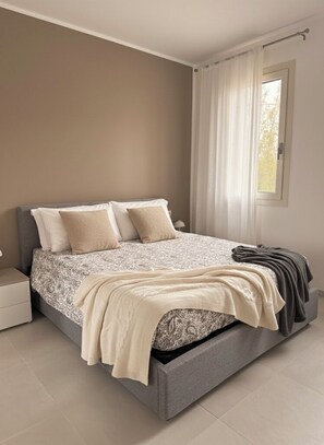 Un dormitorio con cama, mesita de noche y ventana con cortinas.