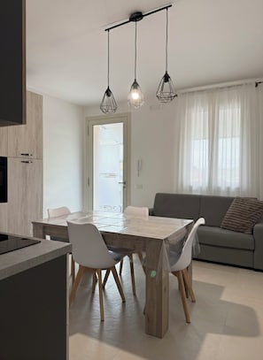 Una cocina moderna con una mesa y sillas de comedor, un sofá gris y lámparas colgantes.