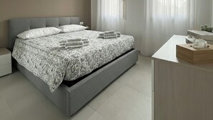Een moderne slaapkamer met een bed, nachtkastjes, een bureau en een raam met gordijnen.