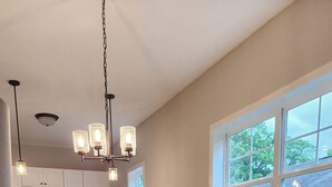 A living room with a yellow armchair, a dining table with chairs, a kitchen in the background, and a large window with a view of trees. - Game-Day Hideaway! Stylish 2BR Near Mercedes-Benz (Atlanta)