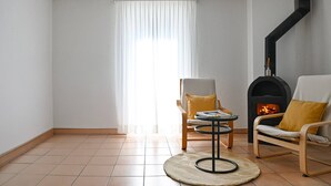 Un salon avec une cheminée, deux fauteuils, une petite table et une fenêtre avec des rideaux.
