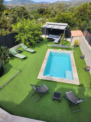 Un jardin avec une piscine, de l’herbe artificielle verte et du mobilier d’extérieur.