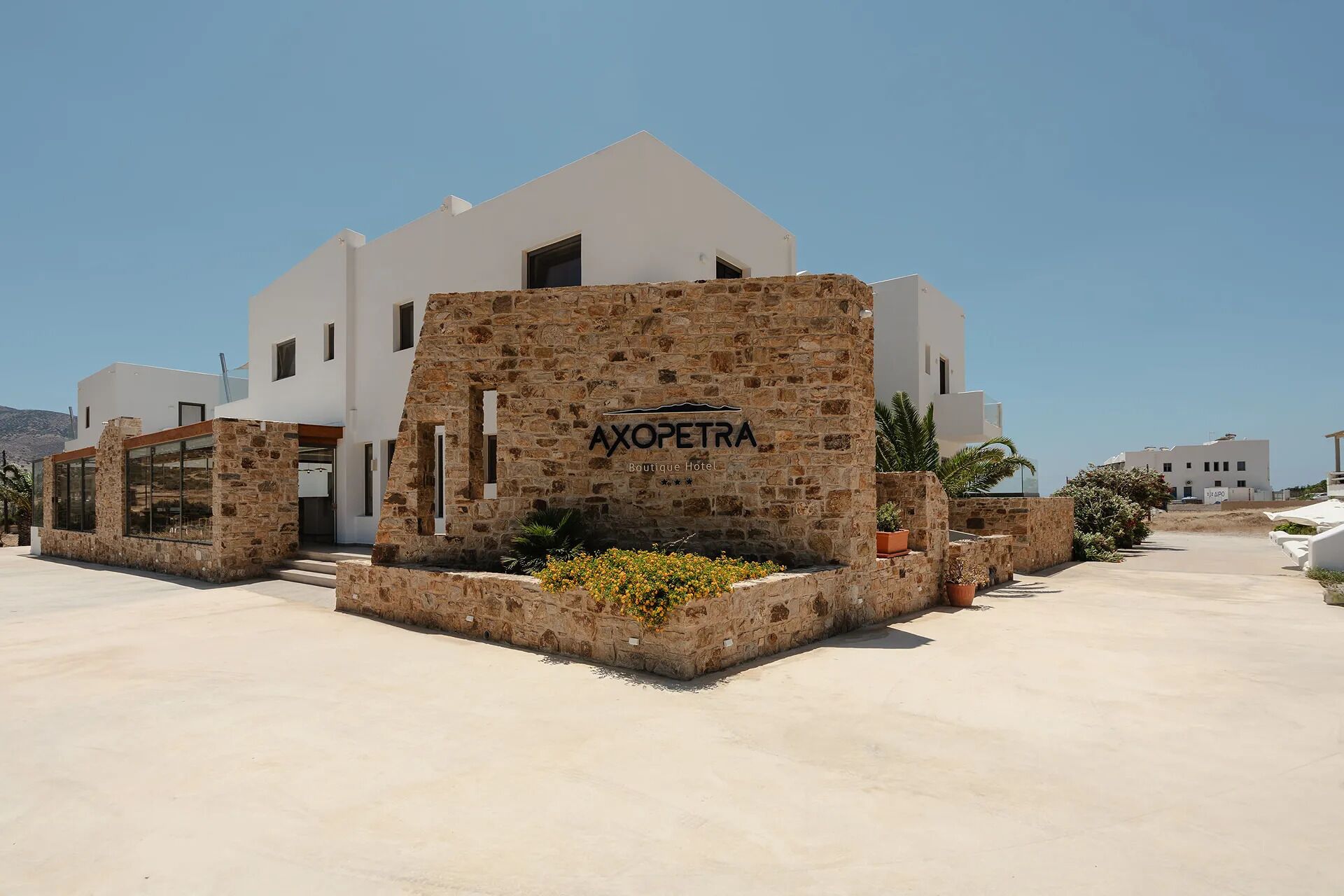 A boutique hotel with a stone facade, a clear sky, and a sign reading 'AXOPETRA Boutique Hotel'.