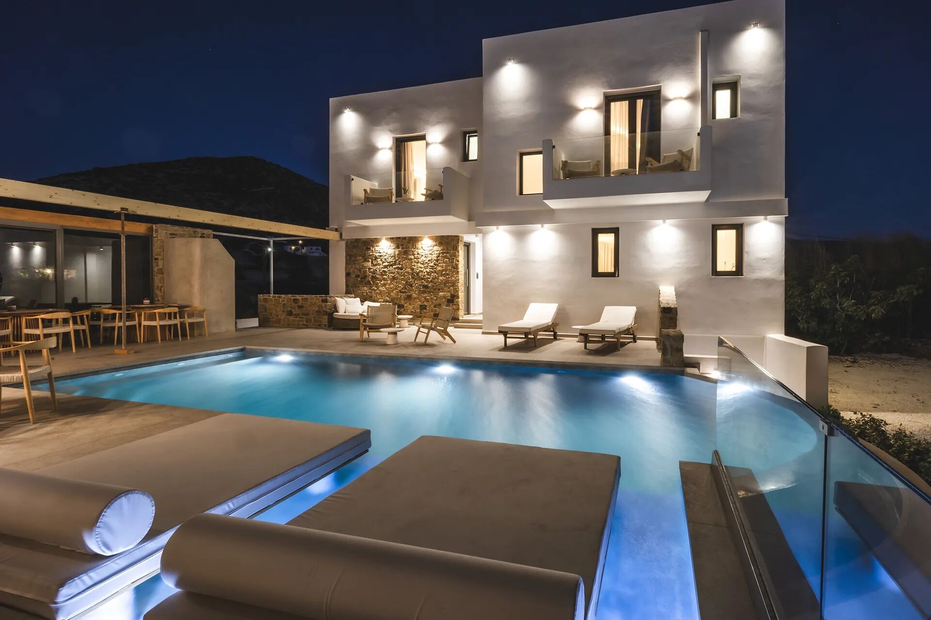 A modern two-story building with a swimming pool, outdoor seating, and a stone wall.