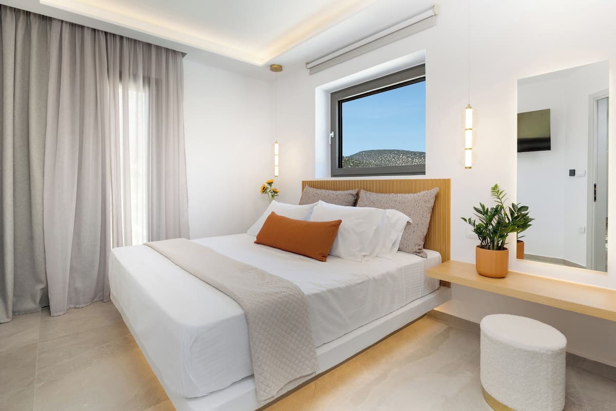 Una habitación de hotel moderna con una cama grande, una mesita de noche con una planta, una ventana con vistas y un televisor de pantalla plana montado en la pared.