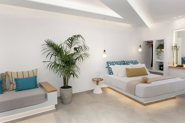 A modern bedroom with a sofa, a bed, a potted plant, and a bedside table.