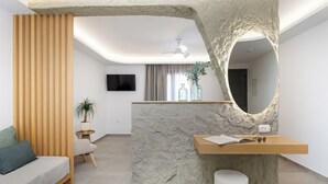 En moderne stue med en sofa, en trævægsafskærmning, en væg med stentekstur, et spejl og et lille bord med en bog og briller.