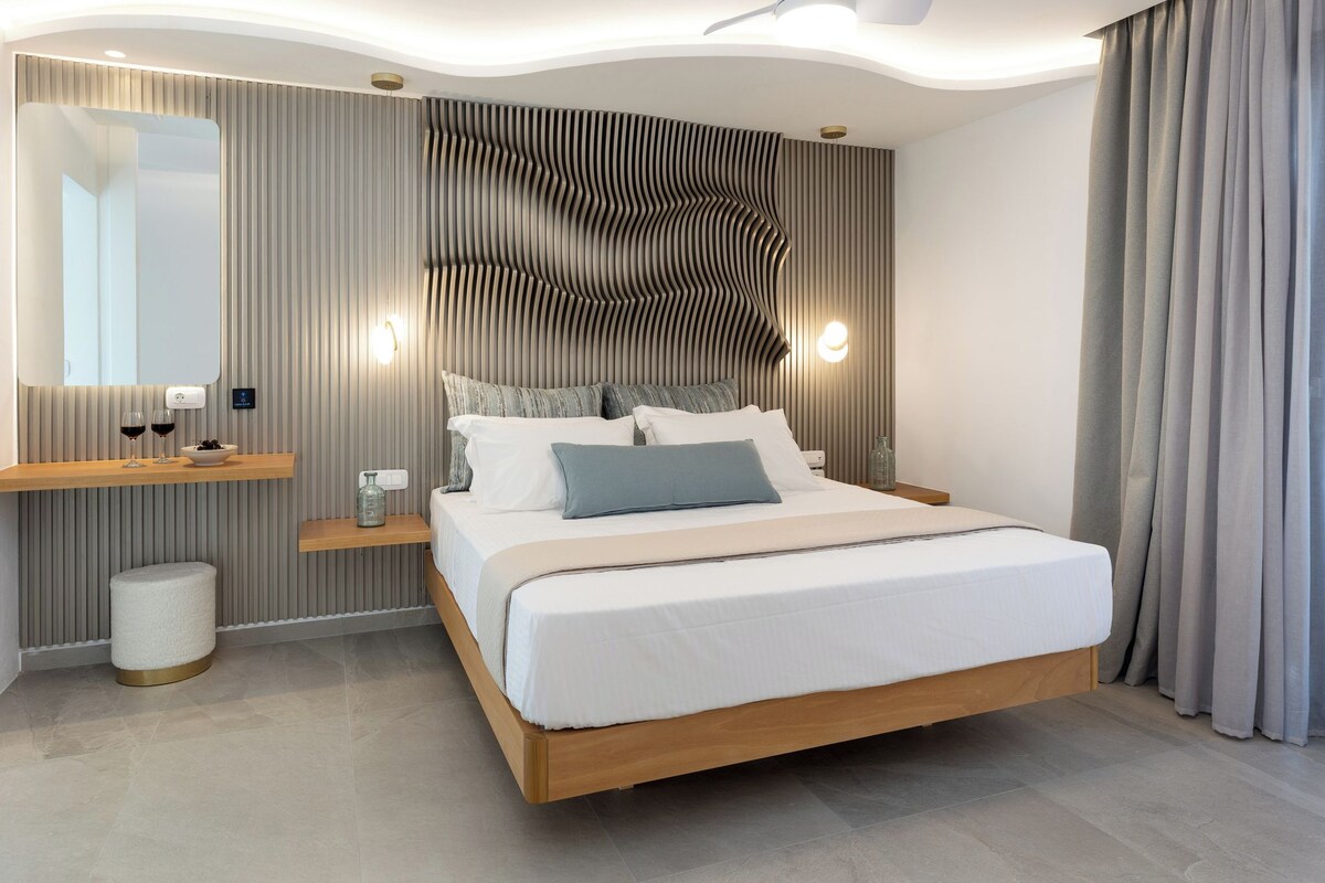 A modern bedroom with a large bed, a bedside table, a mirror, and a wall-mounted light fixture.