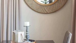 A round mirror with a woven frame on a wall, a table with a candle and a tray, and a chair. - Long Beach Self Catering Two Bedroom Flat (Langstrand)