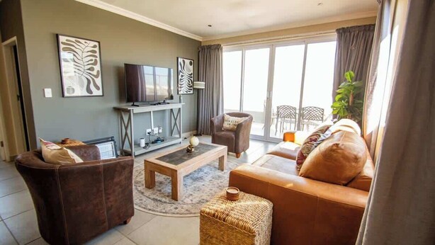 A living room with a sofa, armchair, coffee table, and television. - Long Beach Self Catering Two Bedroom Flat (Langstrand)
