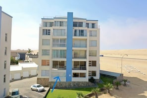 A multi-story hotel with balconies, a parking area, and a view of the beach.
