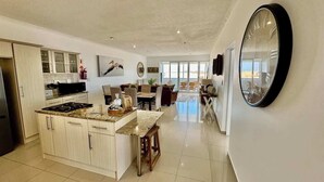 Una cocina amplia con una isla central, un comedor con una mesa grande y una sala de estar con sofá y sillones.