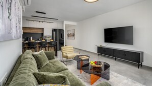 Ein modernes Wohnzimmer mit einer Couch, einem Couchtisch, einem Fernseher und einer Küche im Hintergrund.