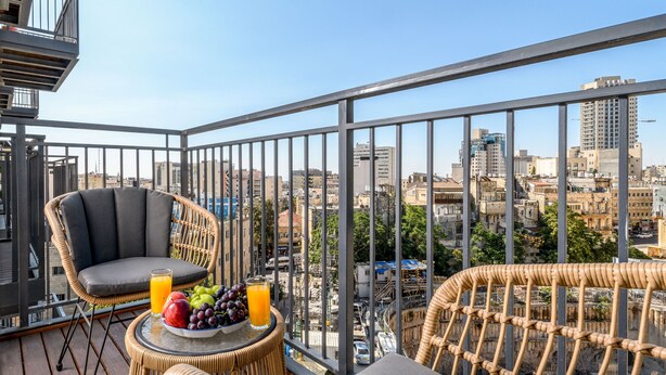 Ein Balkon mit Korbmöbeln, einem Tisch mit Obst und Saft sowie Blick auf die Stadt.