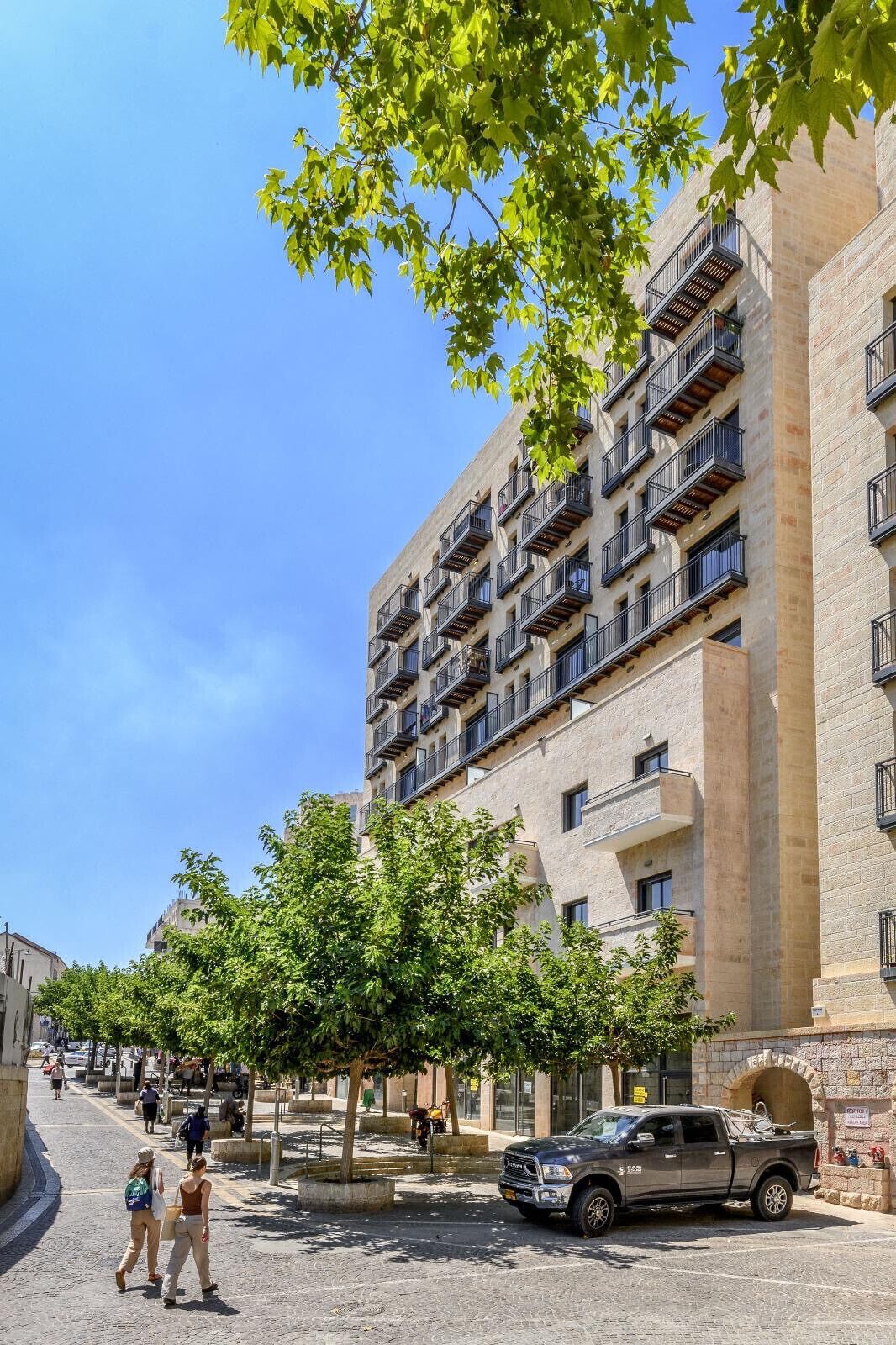 A multi-story building with balconies, a paved street, and pedestrians.