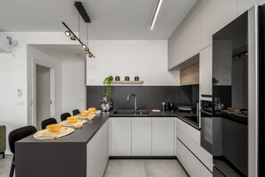 A modern kitchen with a central island, black countertops, and white cabinetry. - Design Apartment City Center with Balcony (Jerusalem)