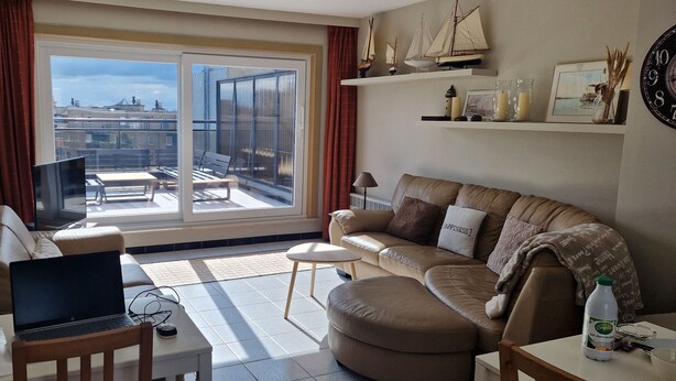 Ein Wohnzimmer mit einer Couch, einem Couchtisch, einem Fernseher und einem Balkon mit Blick auf Gebäude.