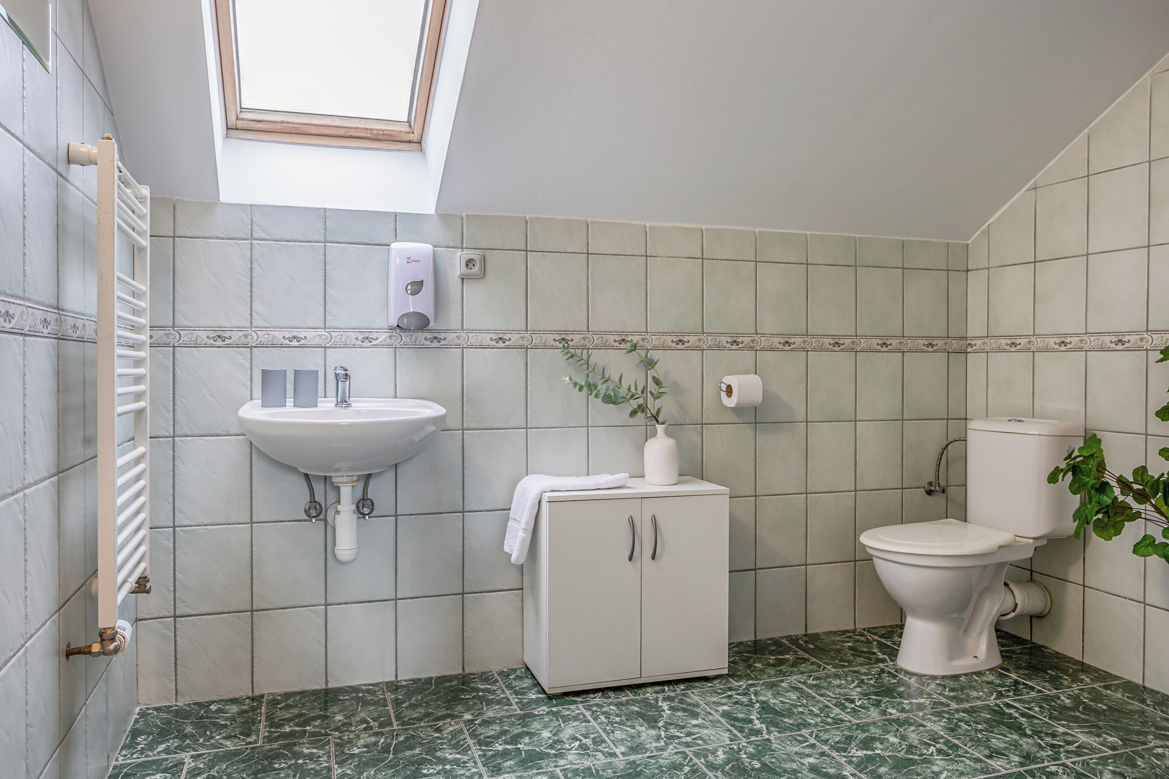 Un bagno con finestra a lucernario, un lavandino, un armadietto e un water.