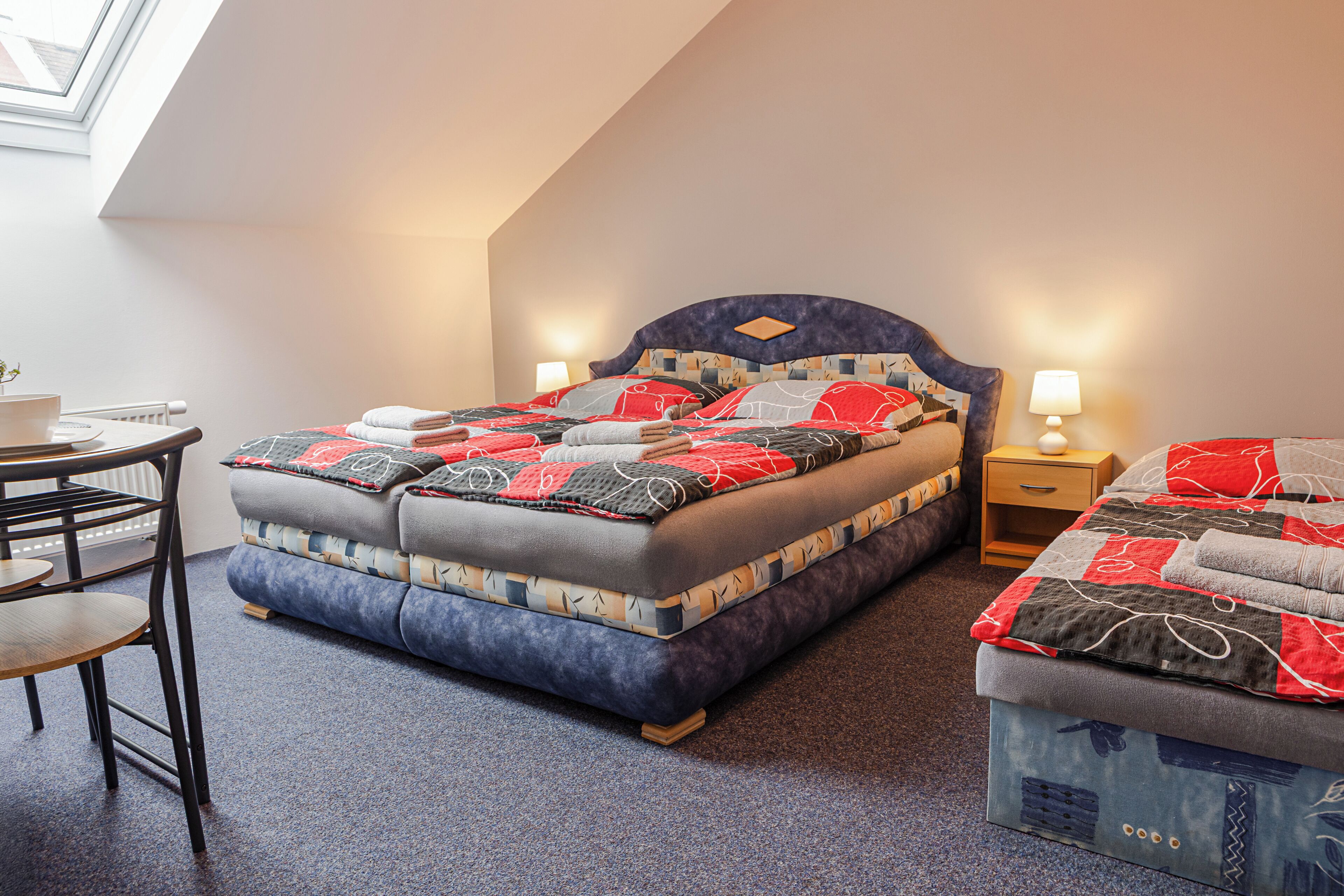 A bedroom with a bed, a desk, a chair, and a nightstand.