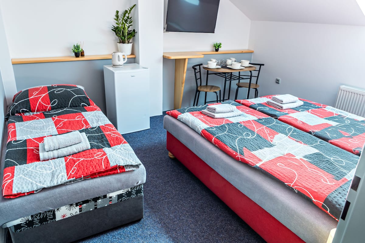 A bedroom with a bed, a desk, a chair, a small refrigerator, and a TV.