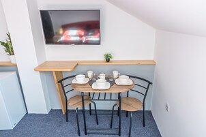 Un pequeño comedor con una mesa preparada para cuatro, un televisor montado en la pared y una planta en maceta al lado.