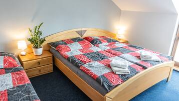 A bedroom with a wooden bed, a nightstand with a lamp, a potted plant, and a blue carpet.