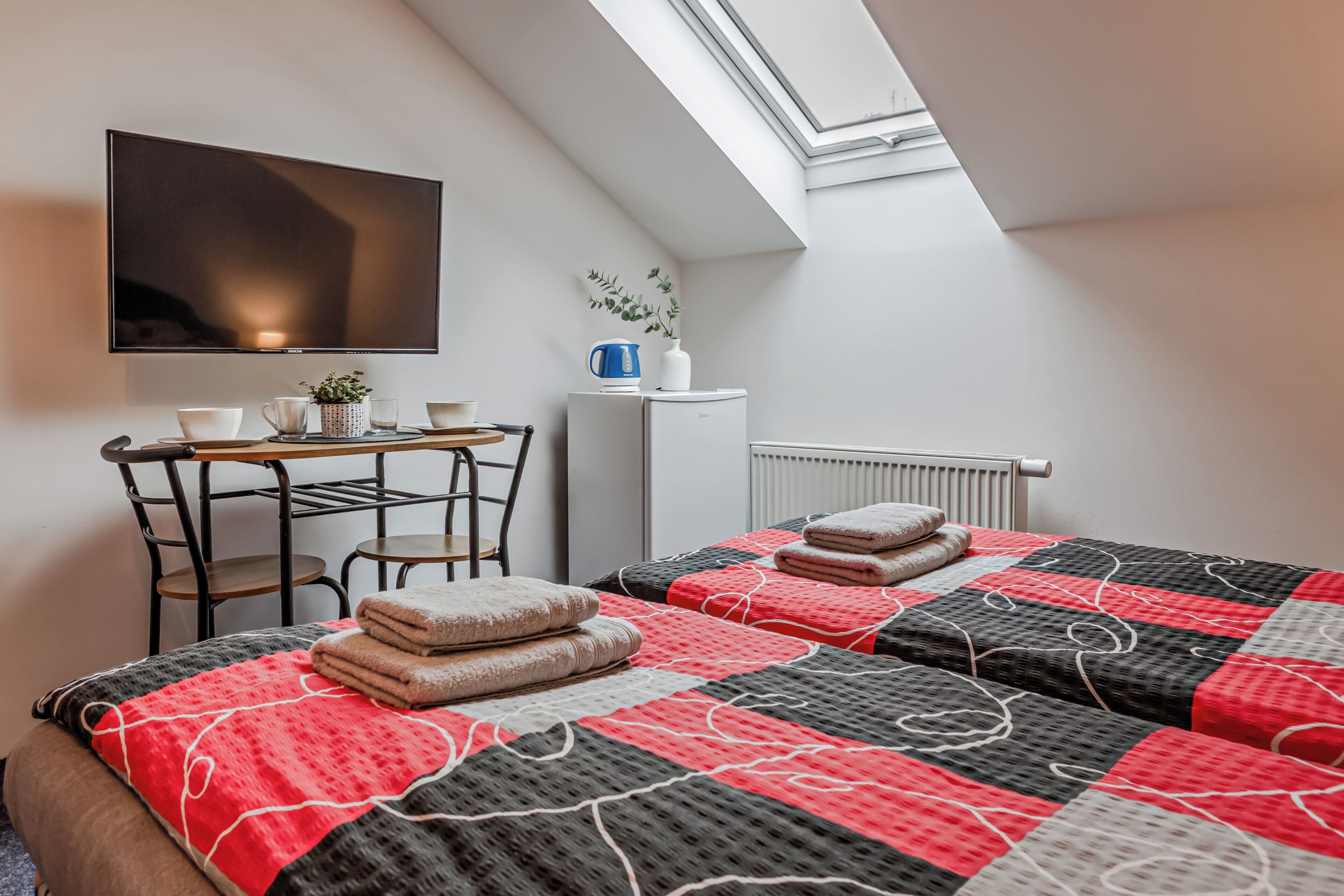 Una habitación con cama, escritorio, silla, radiador y televisor.