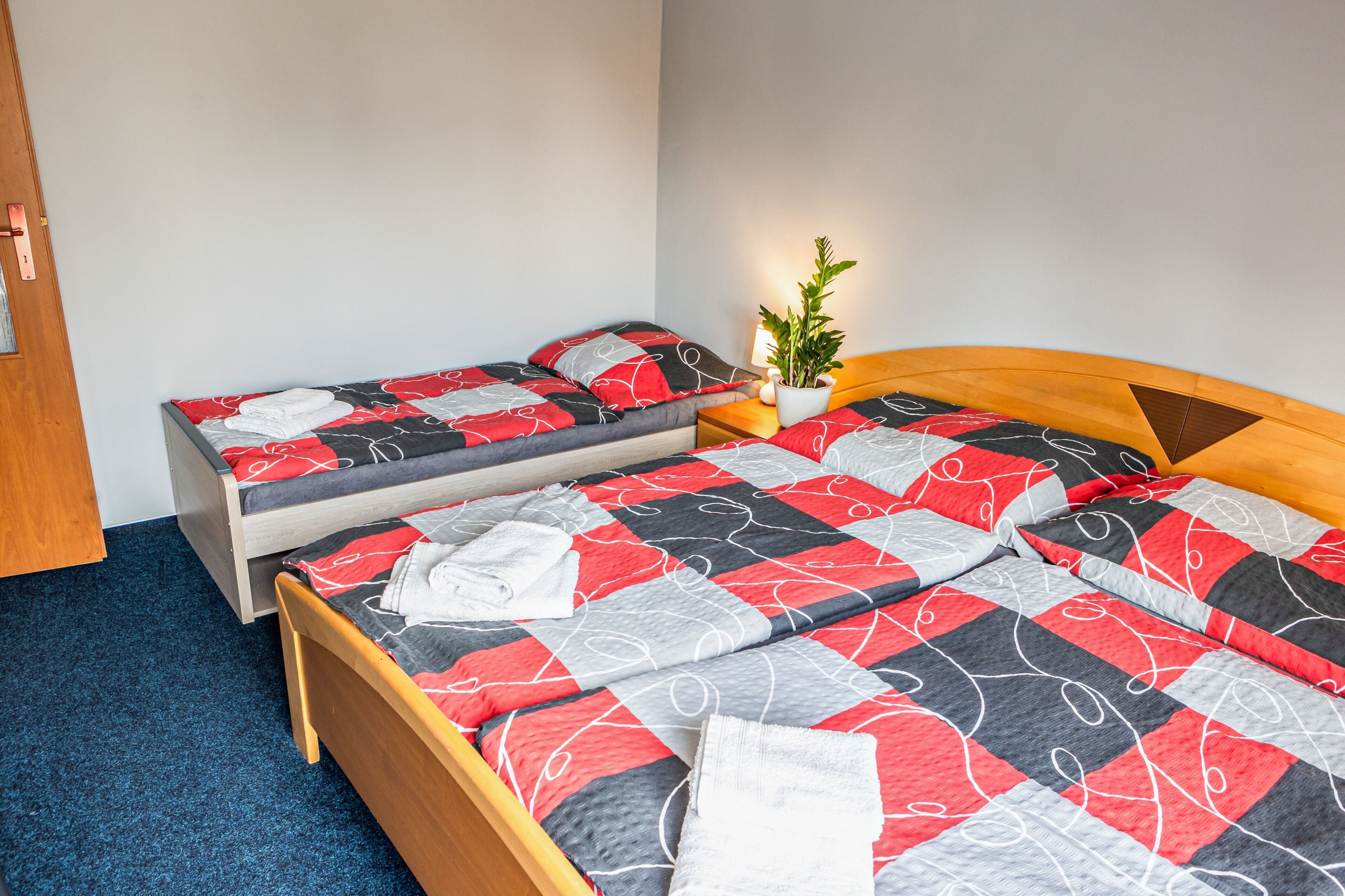 Une chambre avec deux lits, dont un plus grand et un plus petit, tous deux dotés de draps à motifs rouges et gris.