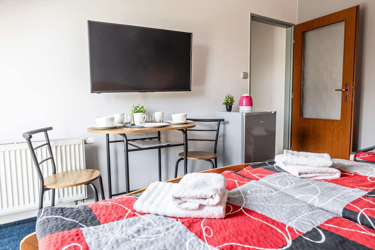 A hotel room with a bed, a TV, a desk with chairs, a coffee machine, and a door.