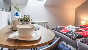 A cozy room with a round wooden table, a bed with a red and black quilt, a potted plant, and a radiator.
