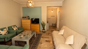 A living room with a sofa, a coffee table, a television, and a plant. - Cozy Apartment in Faliro (Palaio Faliro)