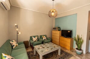 A living room with a sofa, two armchairs, a coffee table, a TV, a cabinet, and a hanging light fixture. - Cozy Apartment in Faliro (Palaio Faliro)