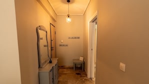 A narrow hallway with a light fixture, a mirror, a coat rack, and a small table with a towel. - Cozy Apartment in Faliro (Palaio Faliro)