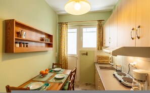 A compact kitchen with wooden cabinets, a dining table set for four, and a window with curtains. - Cozy Apartment in Faliro (Palaio Faliro)