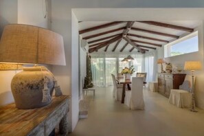 A dining area with a table and chairs, a lamp, and a vase on a wooden table. - ELITE COLLECTION- Cala di Volpe Luxury Villa | Infinity Pool & Sea View (Cala di Volpe)