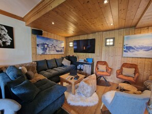 Ein gemütliches Wohnzimmer mit Holzboden, einem großen Flachbildfernseher und zwei Bilderrahmen an der Wand.