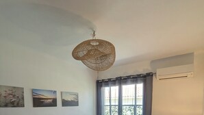 Ein Schlafzimmer mit einem Bett, einem Sessel, einem Tisch mit Lampe und einem Fenster mit Vorhängen.