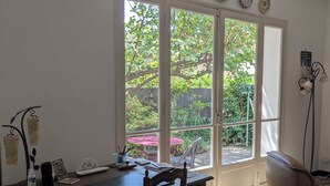 Ein Essbereich mit Tisch und Stühlen, ein Fenster mit Blick ins Grüne und eine Wand-Klimaanlage.