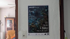 Ein Poster an einer Wand mit Text und einem QR-Code, ein Stuhl, eine Lampe und eine teilweise sichtbare Tür.