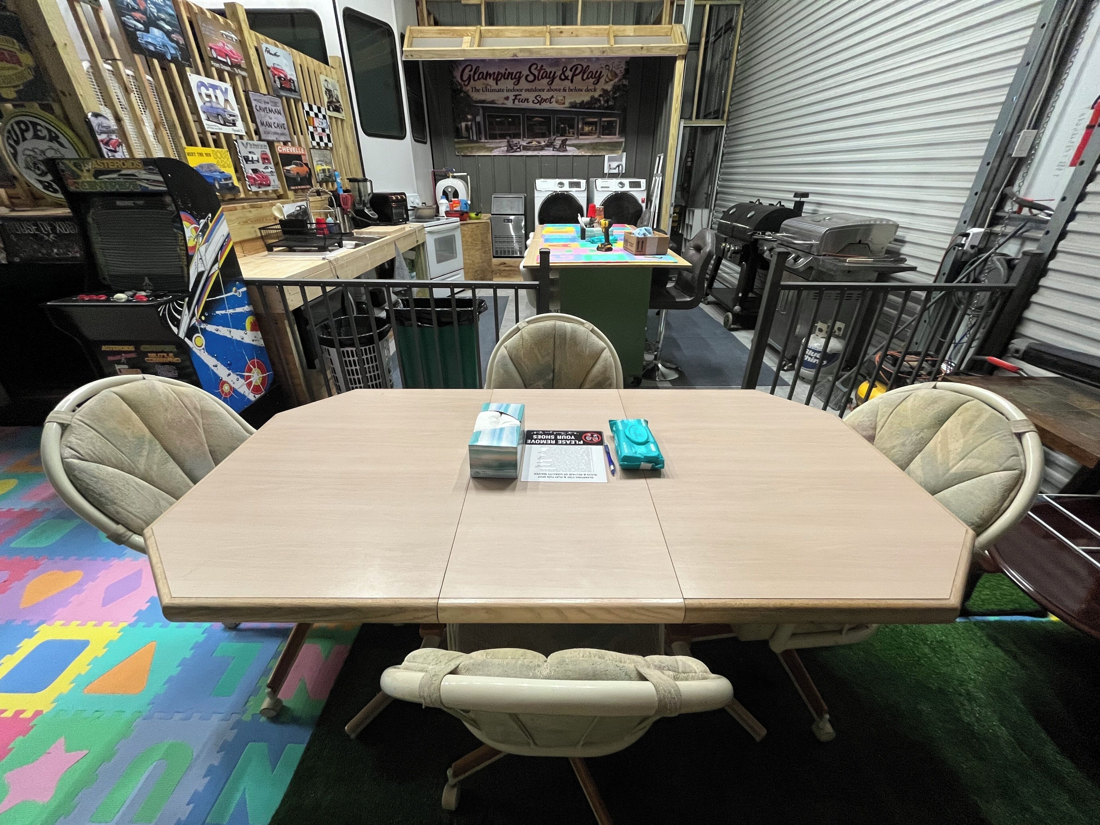 Un espace repas avec une table, des chaises et un coin jeux à l’arrière-plan.