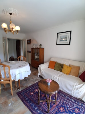 Ein Wohnzimmer mit rundem Tisch, einer Couch, einem gemusterten Teppich, einem Schrank und einer Chandelier.