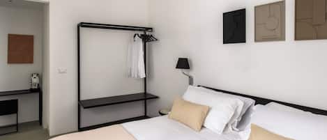 A hotel room with a bed, a bedside table, a lamp, a coat rack, and artwork on the wall.