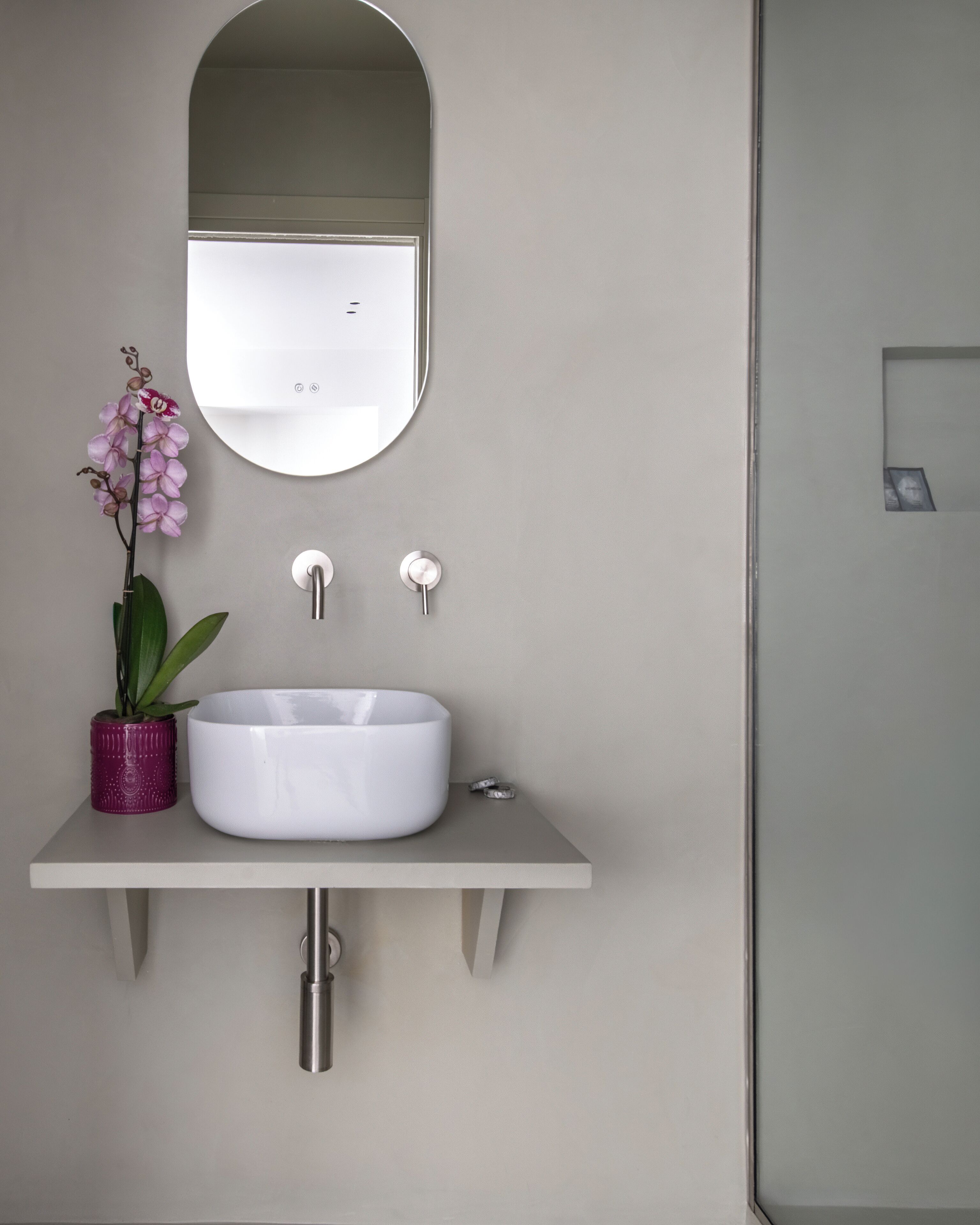 A bathroom with a white sink, a mirror above it, and a potted orchid to the left.